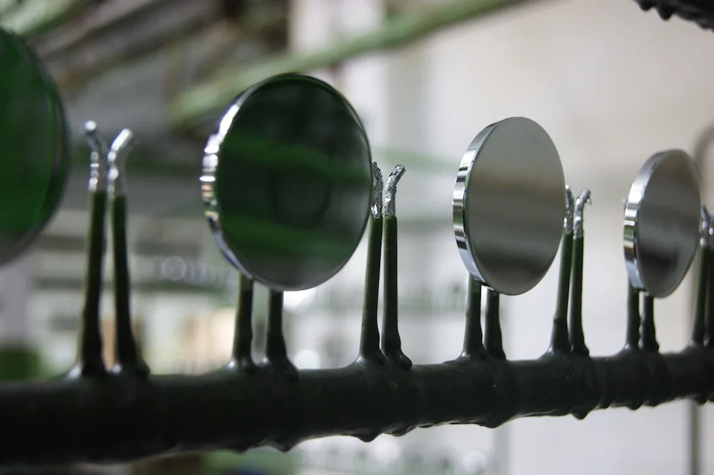 Spiegelnd verchromte Ronden an den isolierten Haken einer Gestellstange in der Galvanik