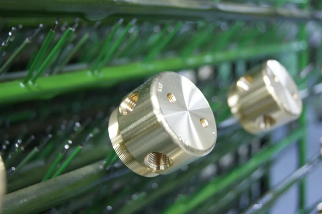 Zylindrische Drehteile mit goldglänzender Oberfläche an den grün isolierten Haken eines Galvanikgestells