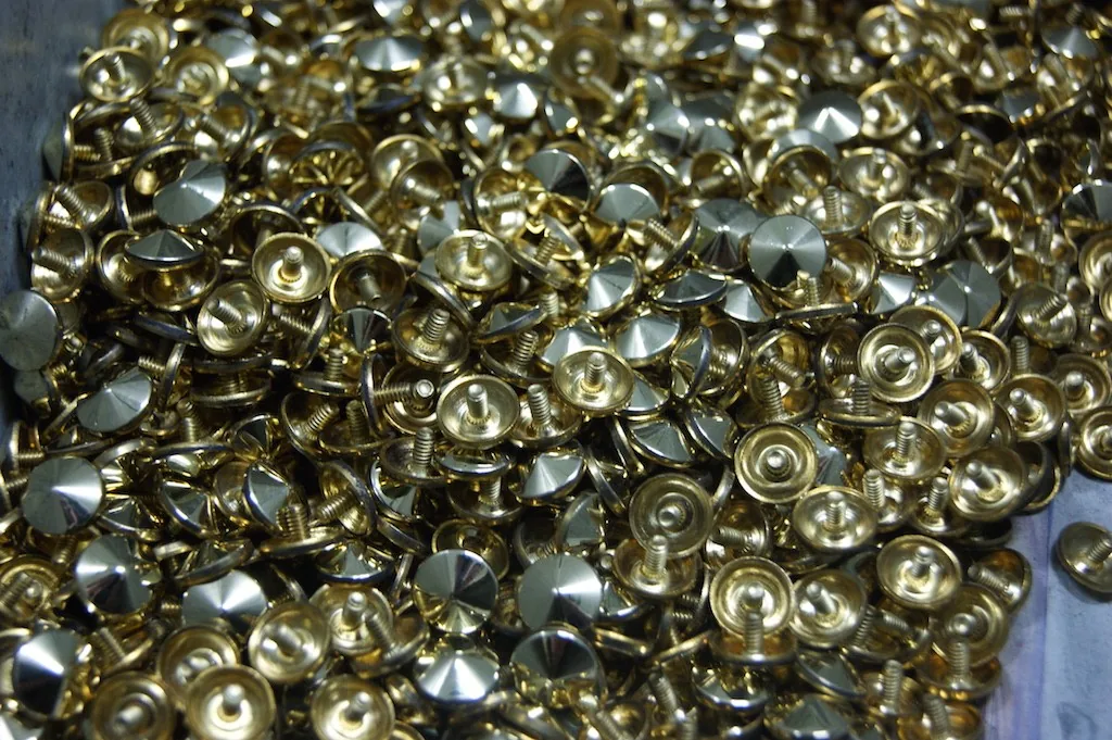 Schüttgut kleiner Schrauben mit poliertem Kegelkopf, teils goldfarben, teils silbrig glänzend, in einer Wanne