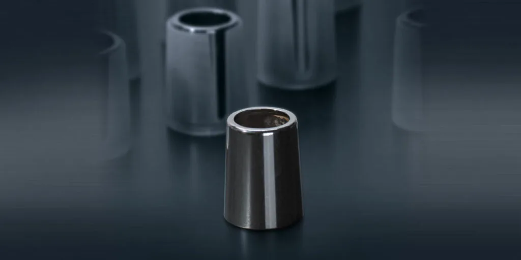 Konische Metallhülse mit spiegelnder Hochglanzoberfläche, weitere Hülsen unscharf im Hintergrund